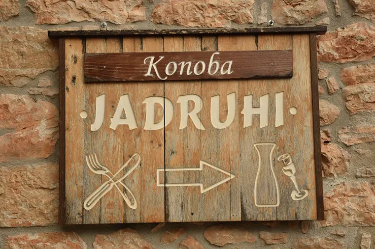 Drveni natpis Konoba Jadruhi na kamenom zidu